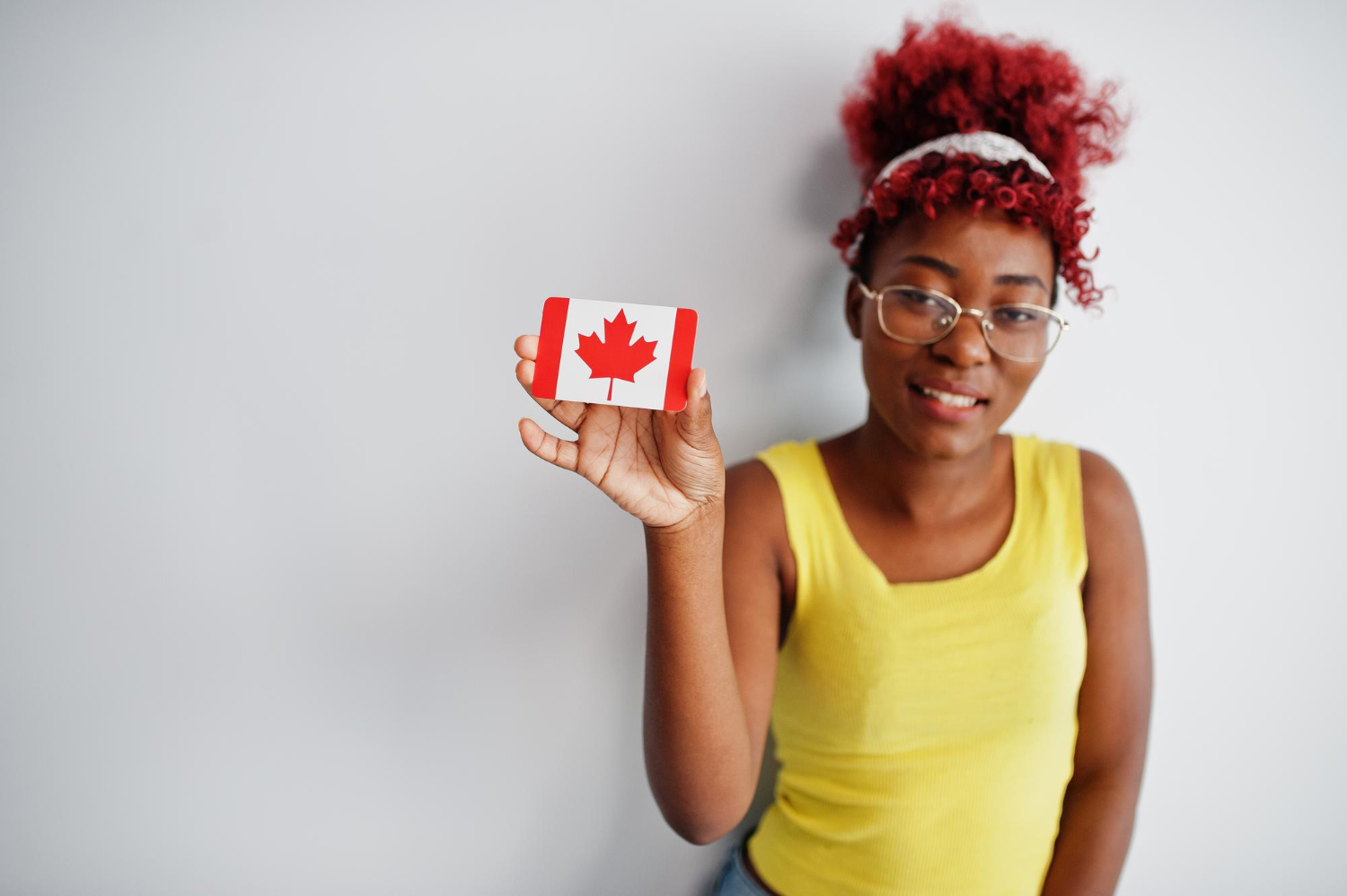 african american woman with afro hair wear yellow singlet eyeglasses hold canada flag isolated white background