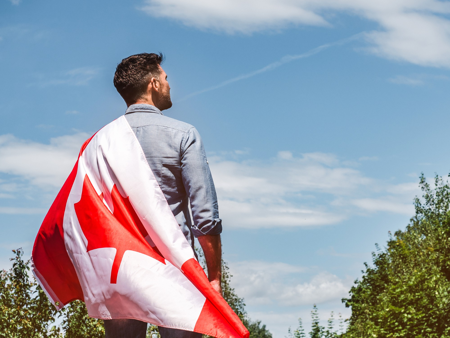 attractive man holding canadian flag blue sky background clear sunny day view from back close up national holiday concept